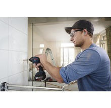 Handwerker bohrt mit einem Akku-Bohrschrauber ein Loch in eine geflieste Wand im Badezimmer.