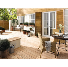 Helle Holzterrasse mit Gartenmöbeln, Pflanzen und dekorativen Elementen vor einem Haus mit Holzfassade