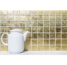 Goldfarbene Mosaikfliesen im Hintergrund mit einer weißen Teekanne im Vordergrund