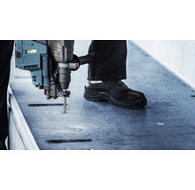 Ein Mann bohrt mit einem Bohrhammer ein Loch in eine Betonoberfläche.