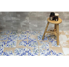 Badezimmergestaltung mit Fliesen in Steinoptik an der Wand und Ornamentfliesen auf dem Boden, sowie einem Hocker mit Dekoration