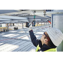 Ein Bauarbeiter montiert mit einem Akku-Bohrschrauber eine Rohrbefestigung an einer Metallstruktur.