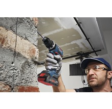 Ein Mann bohrt mit einem Akku-Bohrhammer in eine Ziegelwand.