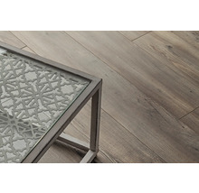 Detailansicht eines Tisches mit Glasplatte und dekorativem Muster, daneben ein Holzboden.