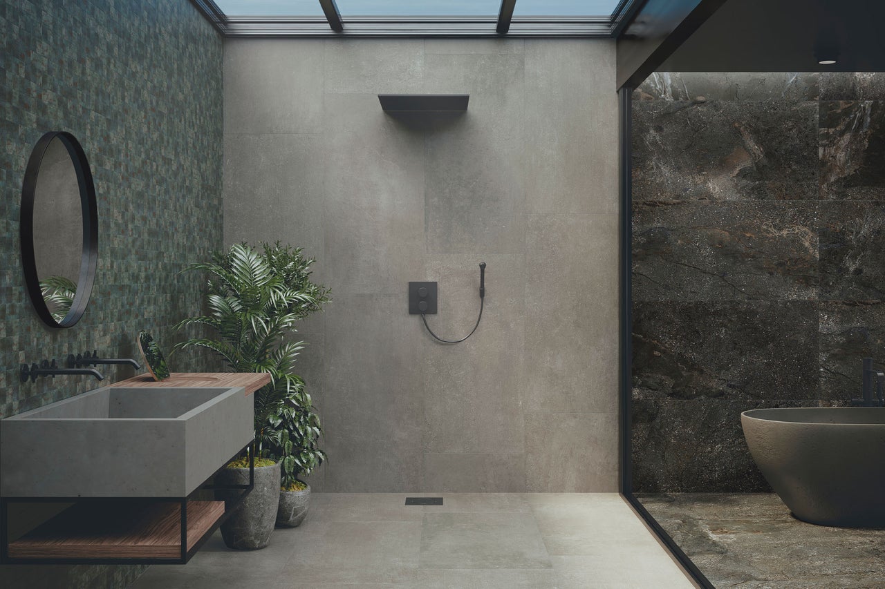 Modernes Badezimmer mit Oberlicht, großformatigen Wandfliesen, Mosaikwand, Betonwaschbecken, runder Spiegel und freistehender Badewanne.
