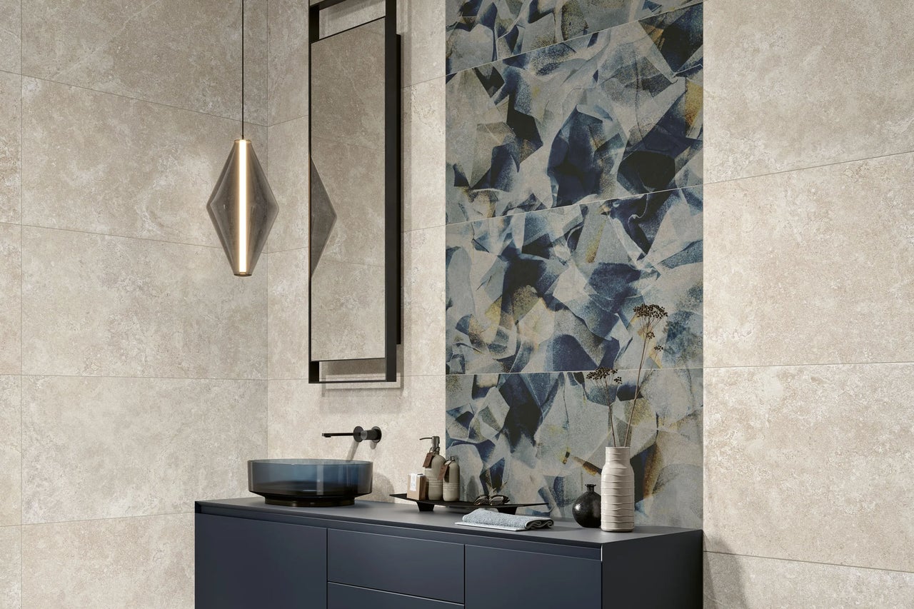 Modernes Badezimmer mit dunkelblauem Waschtischunterschrank, blauem Glaswaschbecken, beigen Wandfliesen in Steinoptik und blauer Akzentfliese.