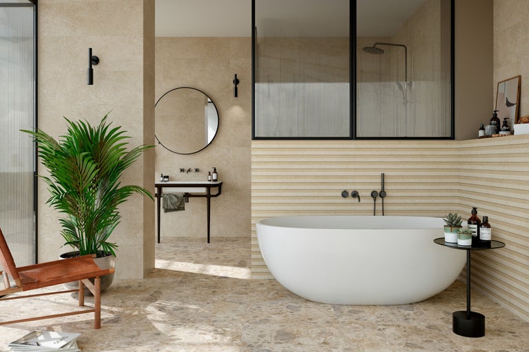 Modernes Badezimmer mit freistehender weißer Badewanne, beigen Wandfliesen in Lamellenoptik, Natursteinboden, rundem Spiegel und schwarzen Armaturen.