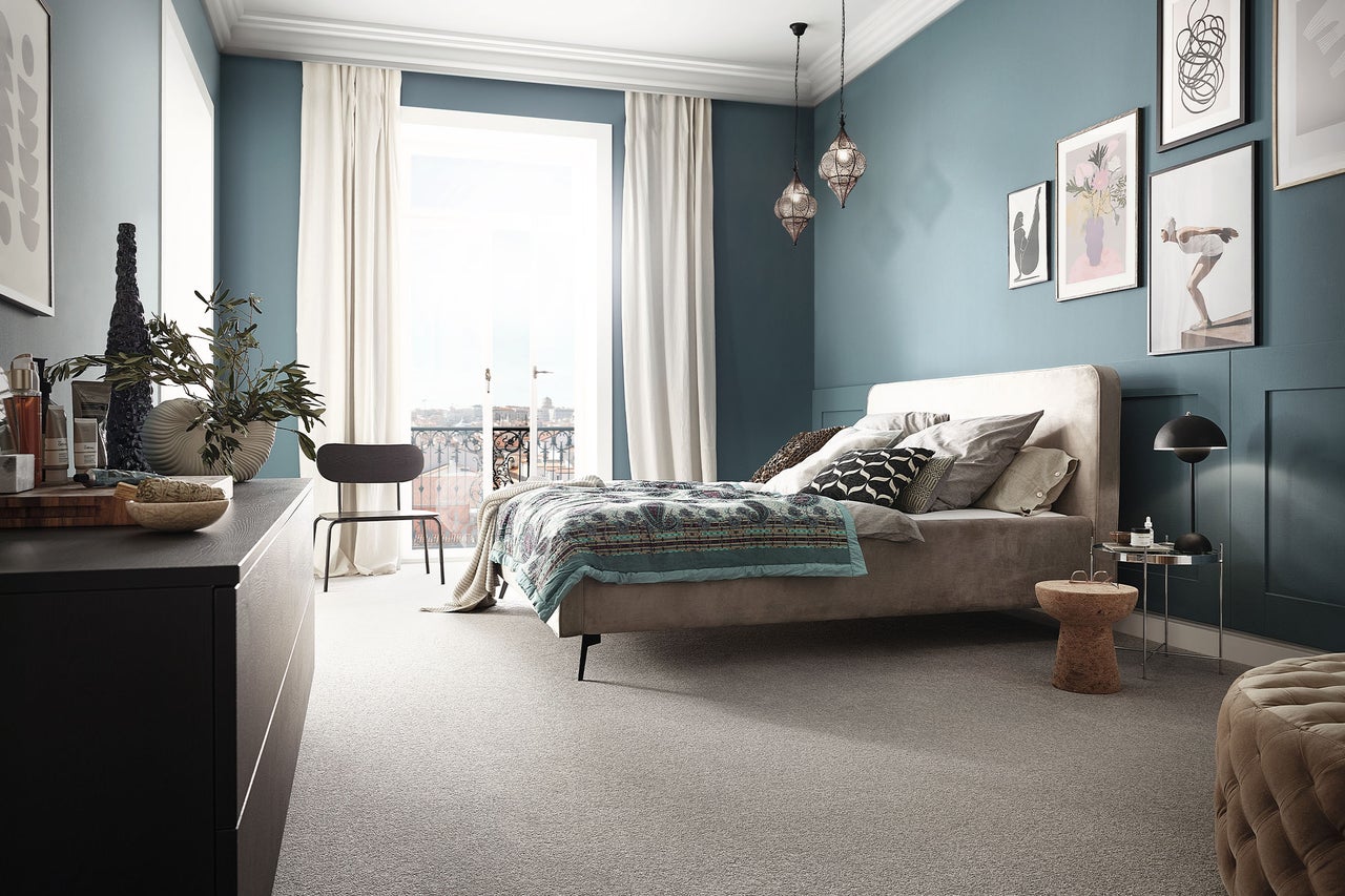 Modernes Schlafzimmer mit blauen Wänden, grauem Teppichboden, einem Doppelbett und großen Fenstern mit hellen Vorhängen.