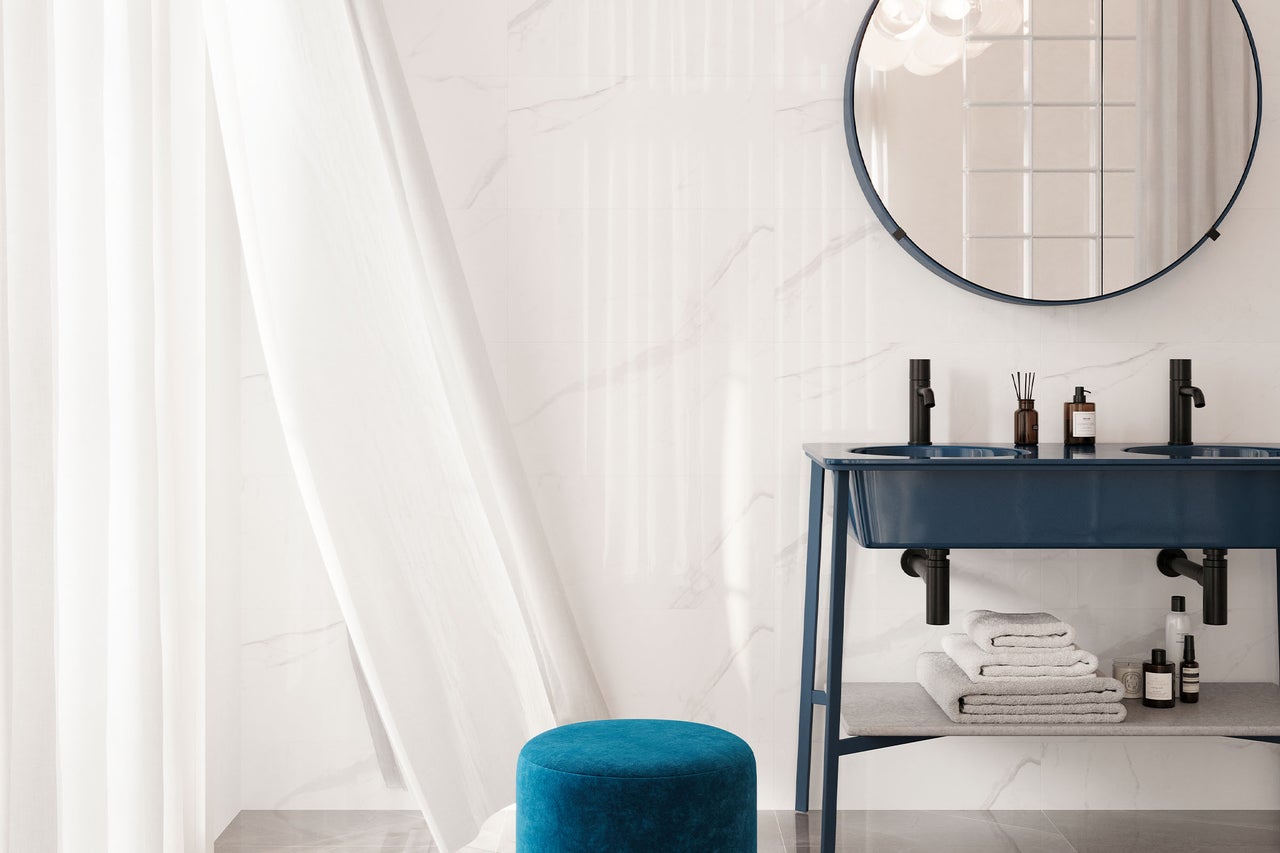 Modernes helles Badezimmer mit dunkelblauem Doppelwaschtisch, zwei schwarzen Armaturen, rundem Spiegel und weißen Wandfliesen in Marmoroptik.