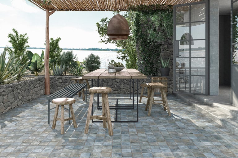 Terrasse mit Holztisch, Hockern und Steinbodenfliesen im Außenbereich.