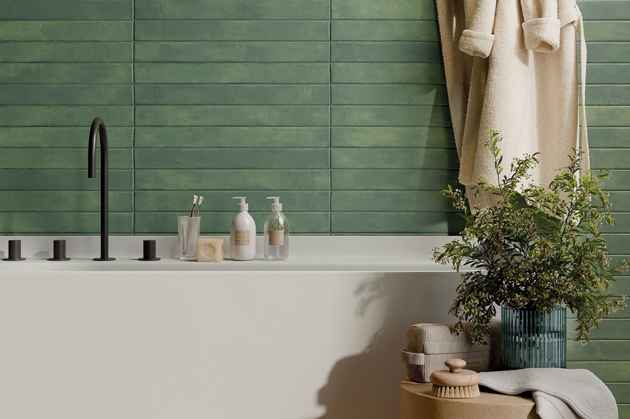 Modernes Badezimmer mit länglichen grünen Wandfliesen, einer weißen Badewanne mit schwarzer Armatur sowie verschiedenen Badutensilien.