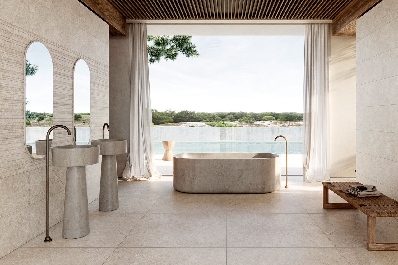 Großzügiges Badezimmer mit freistehender Stein-Badewanne, zwei Säulenwaschbecken und hellen Natursteinfliesen.