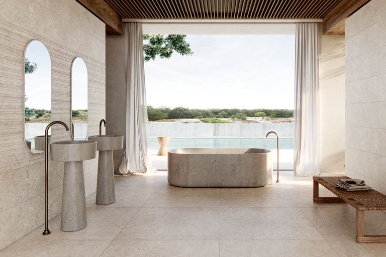 Großzügiges Badezimmer mit freistehender Stein-Badewanne, zwei Säulenwaschbecken und hellen Natursteinfliesen.