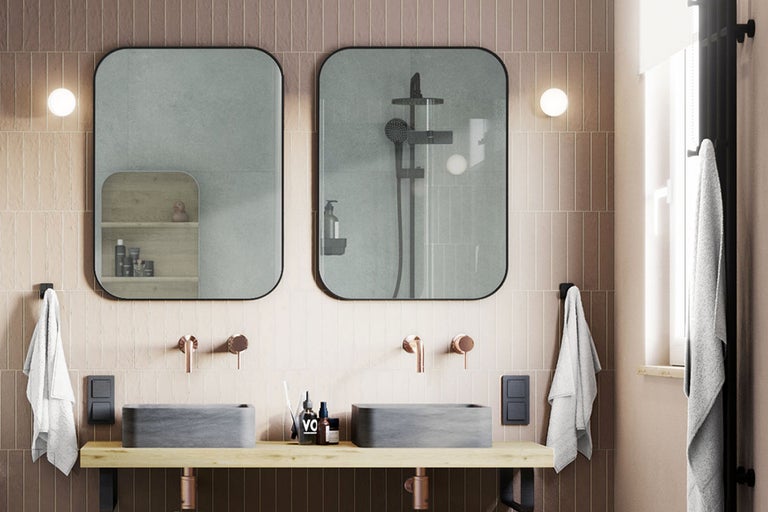 Modernes Badezimmer mit zwei grauen Stein-Aufsatzwaschbecken auf Holzplatte, Kupferarmaturen und zwei abgerundeten Spiegeln vor schmalen Wandfliesen.