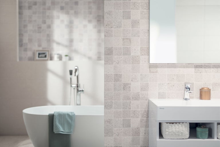 Modernes Badezimmer mit freistehender Badewanne, Waschtischunterschrank und Wandgestaltung mit quadratischen Mosaikfliesen in Steinoptik.