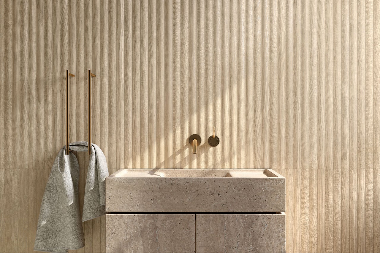 Wandfliesen in Holzoptik mit vertikaler Lamellenstruktur in einem modernen Badezimmer mit Naturstein-Waschtisch und goldener Armatur.