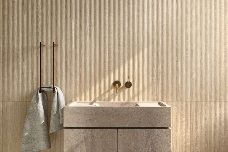 Wandfliesen in Holzoptik mit vertikaler Lamellenstruktur in einem modernen Badezimmer mit Naturstein-Waschtisch und goldener Armatur.