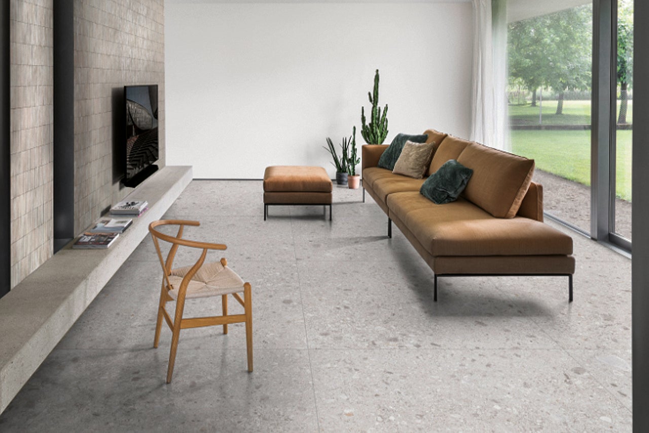 Wohnzimmer mit Bodenfliesen in Terrazzooptik, Sofa, Sessel und Zimmerpflanzen für eine helle und freundliche Atmosphäre.