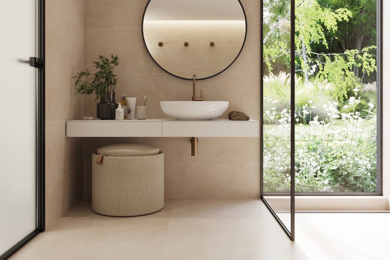 Helles Badezimmer mit Waschbecken, Spiegel und Sitzhocker vor dem Fenster.