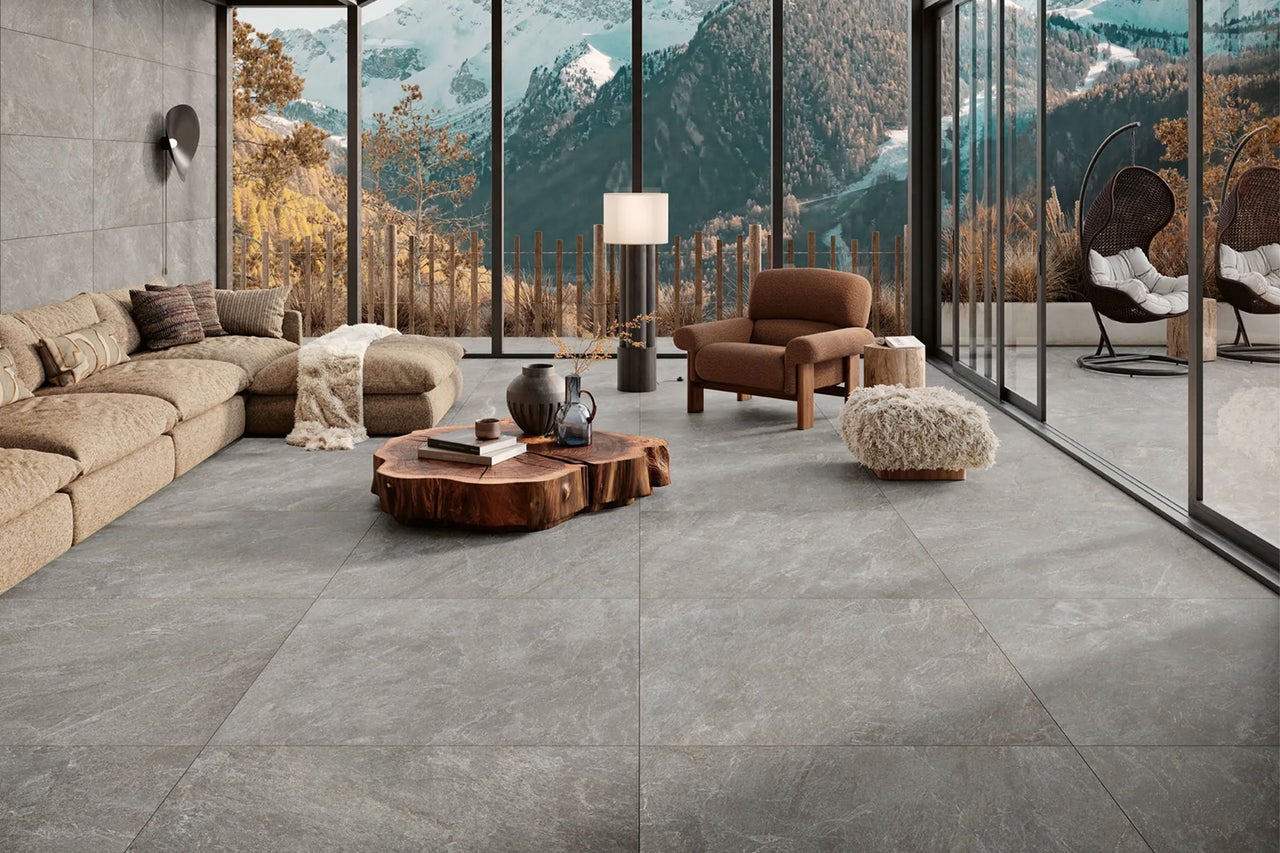 Modernes Wohnzimmer mit großformatigen grauen Bodenfliesen in Steinoptik, Holz-Couchtisch und Panoramafenstern mit Bergblick.