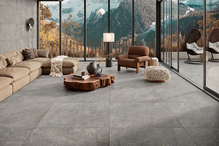 Modernes Wohnzimmer mit großformatigen grauen Bodenfliesen in Steinoptik, Holz-Couchtisch und Panoramafenstern mit Bergblick.