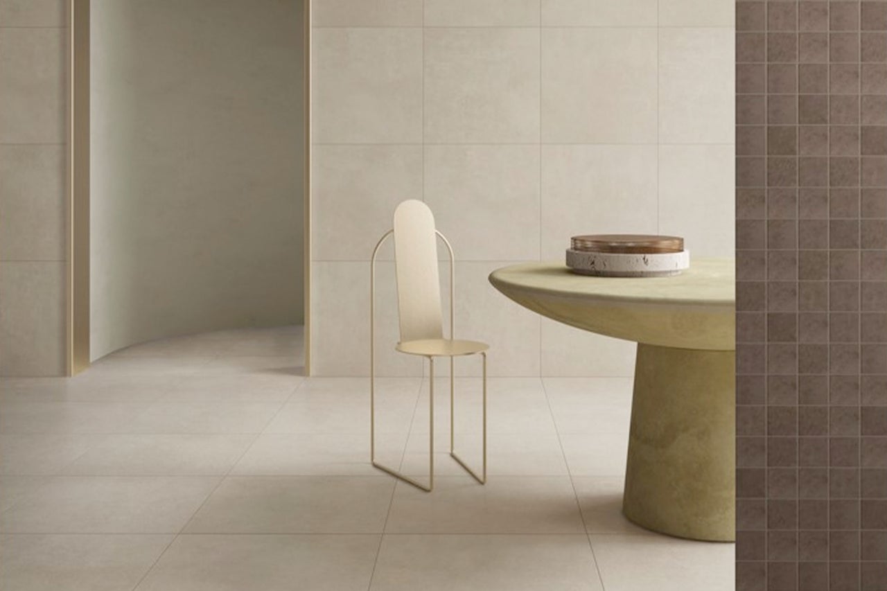 Heller minimalistischer Raum mit Wand- und Bodenfliesen aus Feinsteinzeug, rundem Steintisch, Metallstuhl und Mosaikfliesen an einer Wand.