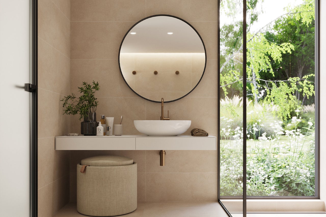 Modernes Badezimmer mit weißem Aufsatzwaschbecken auf weißer Konsole, rundem Wandspiegel und goldener Armatur vor einem Fenster mit Gartenblick.