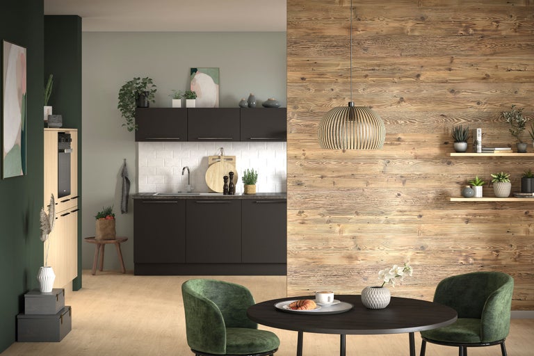 Moderne Küche mit anthrazitfarbenen Schränken, Holzwandverkleidung, Esstisch mit grünen Samtsesseln und einer Pendelleuchte aus Holz.