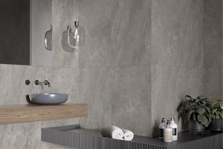 Modernes Badezimmer mit grauen Fliesen, Waschbecken, Spiegel und Handtüchern.