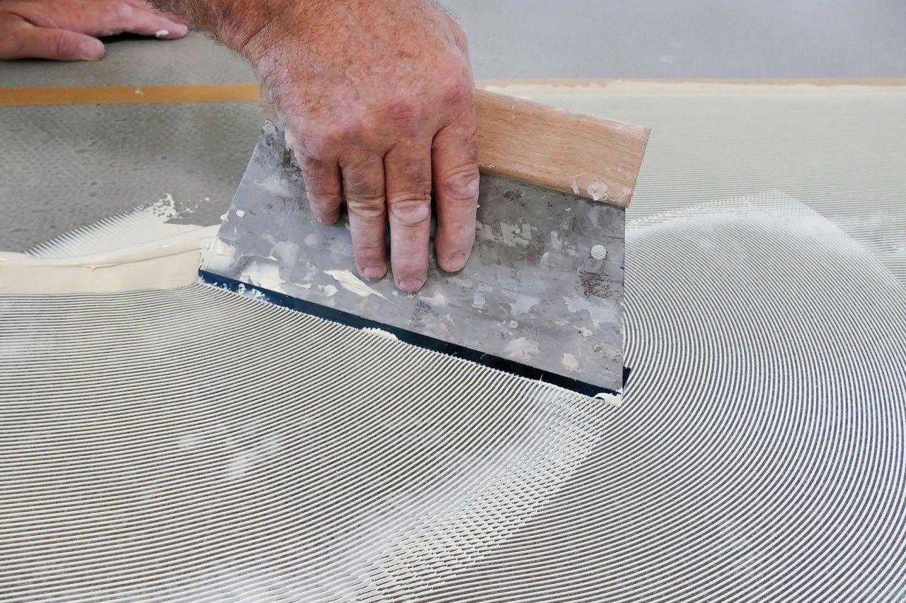Anwendung eines Zahnspachtels zum gleichmäßigen Auftragen von Bodenkleber auf einen Untergrund.
