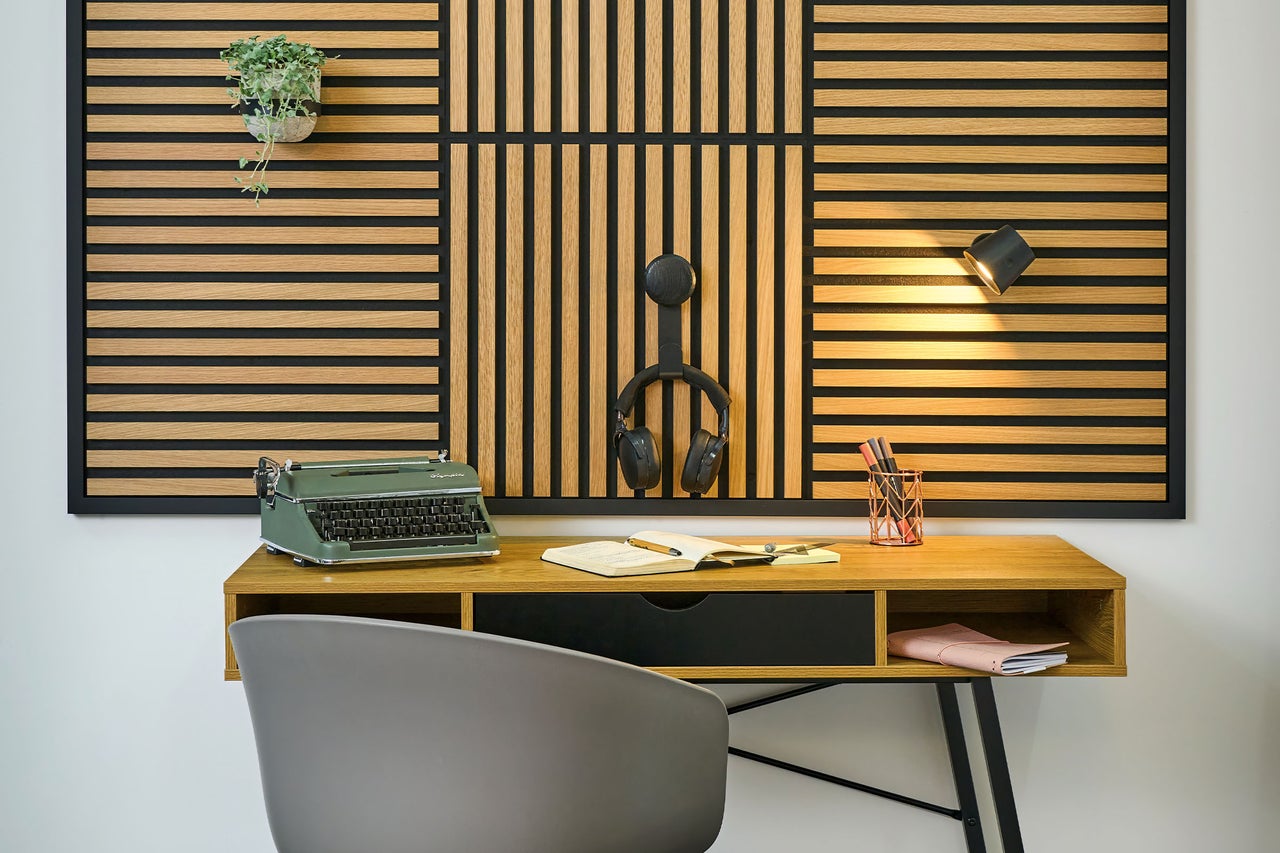 Ein organisierter Arbeitsplatz mit einem hölzernen Wandpaneel aus Lamellen, einem Schreibtisch mit Schreibmaschine und einem grauen Stuhl.