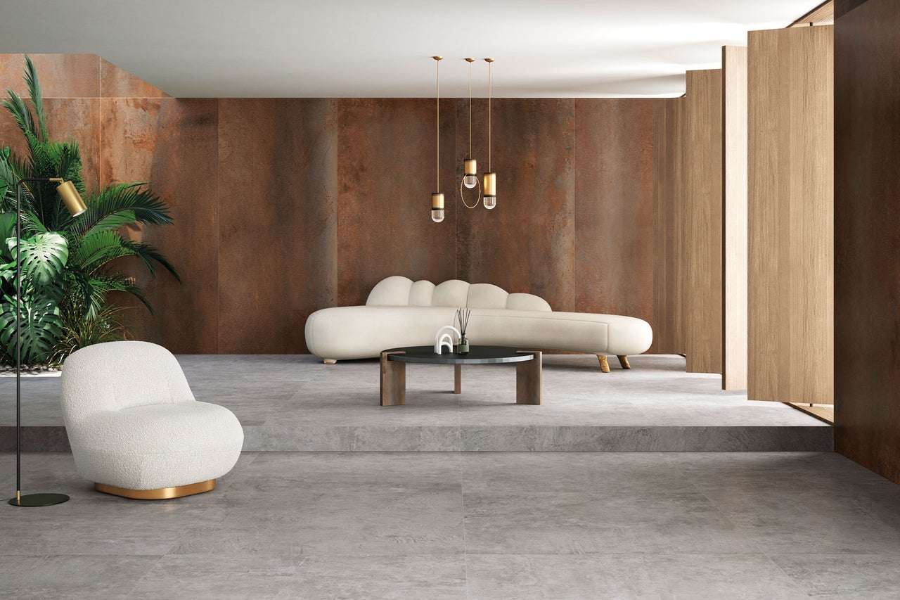Modernes Wohnzimmer mit Bodenfliesen in Betonoptik und Wandfliesen in Rostoptik, weißes Sofa und Sessel, dekorative Pendelleuchten und Zimmerpflanze.