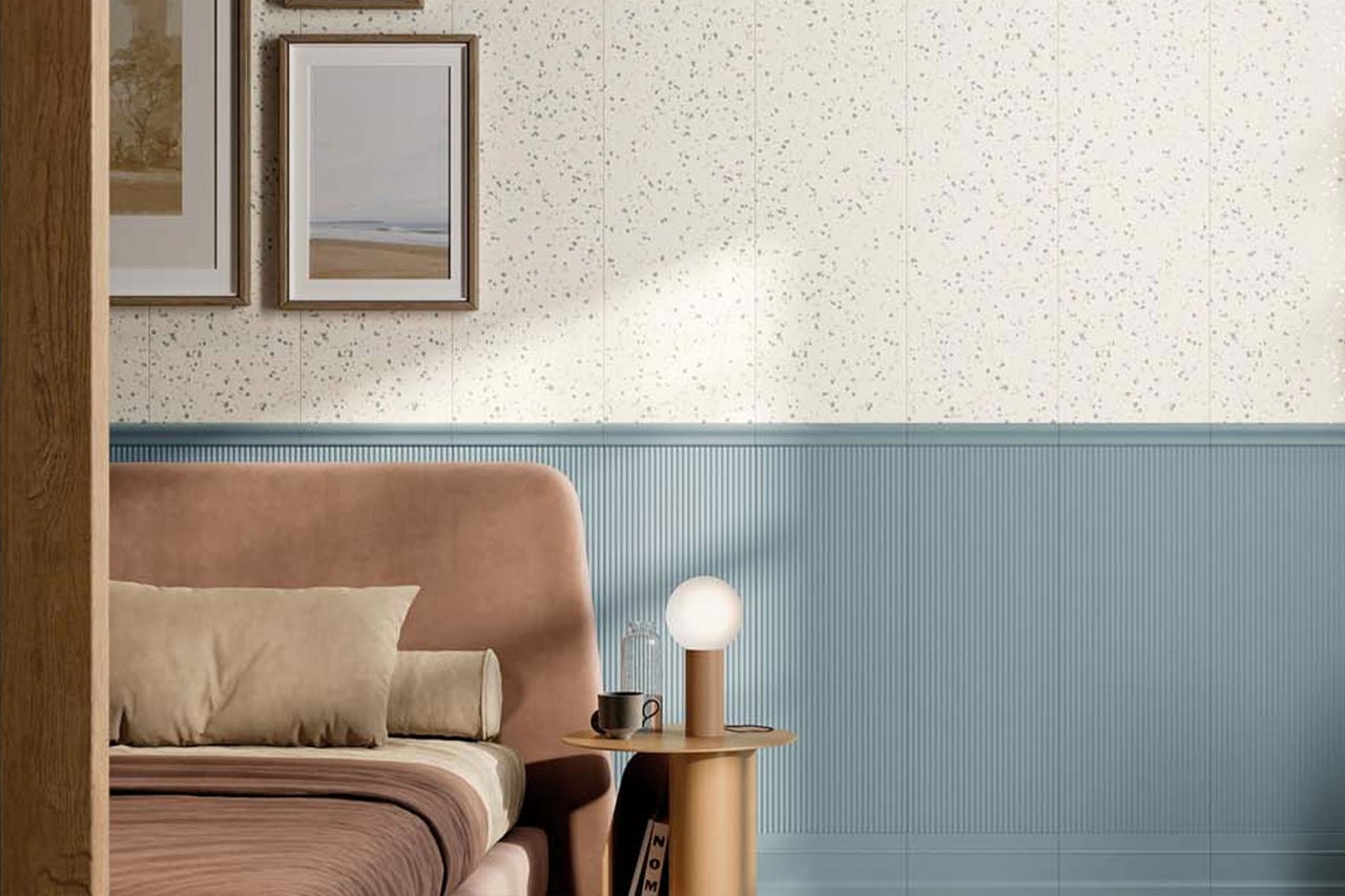 Schlafzimmerwand mit hellen Fliesen in Terrazzo-Optik oben und blauen Wandpaneelen mit vertikaler Riffelstruktur unten.