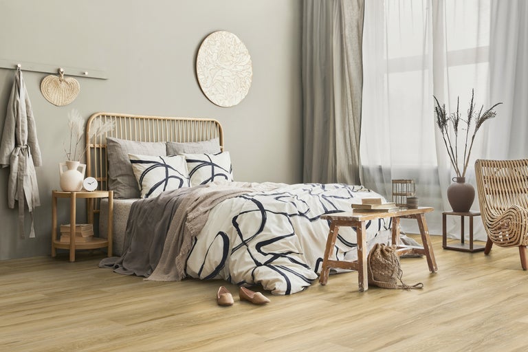 Helles Schlafzimmer mit Holzboden, Rattandekoration und einem Bett mit gemusterter Bettwäsche