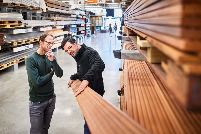 Zwei Männer betrachten Holzbretter im Baumarktregal.