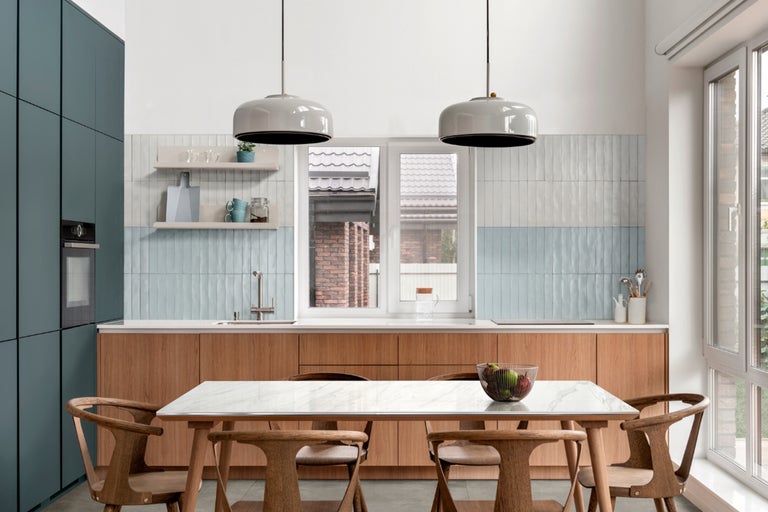 Helle Küche mit Esstisch, Stühlen, Küchenschränken und Beleuchtung.