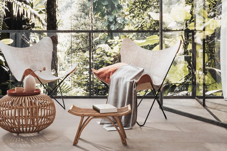 Helle, freundliche Terrasse mit zwei Faltstühlen, Rattantisch und Bambushocker vor einer Glaswand mit Blick ins Grüne