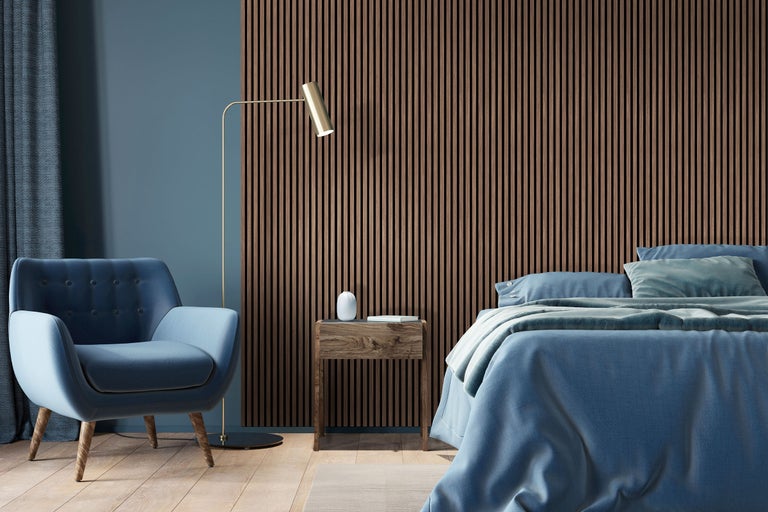 Akustikpaneel aus Holzlamellen an einer Wand in einem modern eingerichteten Schlafzimmer mit Sessel und Stehlampe.