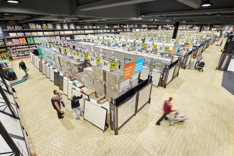 Große Halle im Hornbach Baumarkt mit Fliesenausstellung, Preisschildern und Kunden.