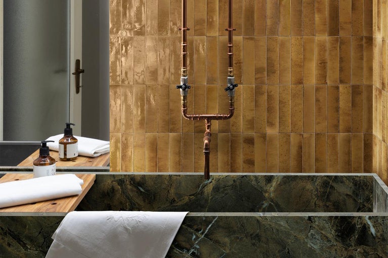 Badezimmer mit Fliesenwand, Kupferrohren und Badewanne aus Marmor