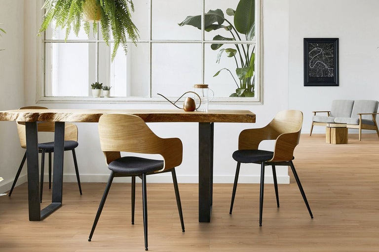 Heller Essbereich mit Massivholztisch, modernen Holzstühlen mit dunklen Polstern und einem Bodenbelag in Holzoptik vor einem großen Fenster.