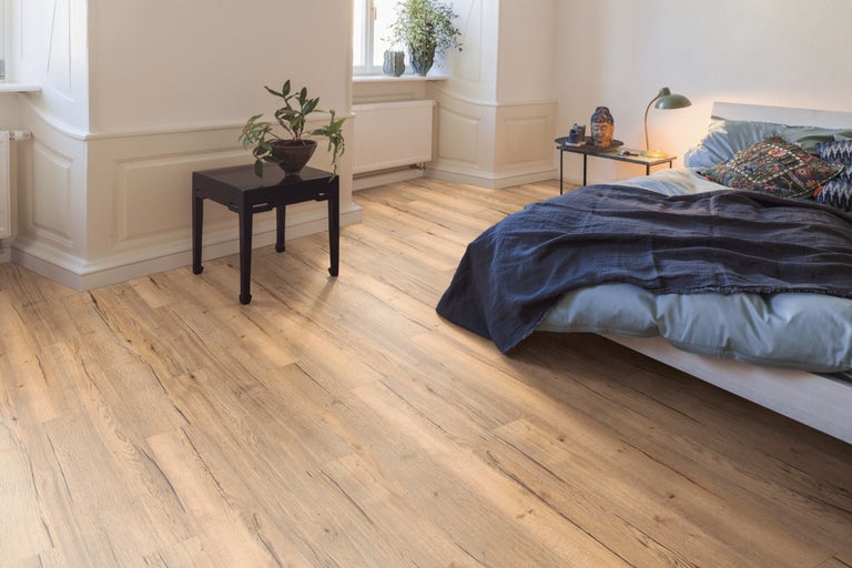 Heller Schlafraum mit Holzboden, Bett, Nachttisch und Zimmerpflanzen.