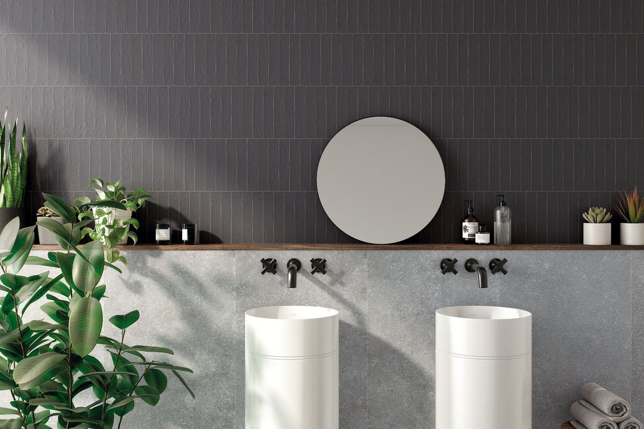 Modernes Badezimmer mit zwei weißen Standwaschbecken, schwarzen Wandarmaturen, einem runden Spiegel und dunkelgrauen vertikalen Fliesen.