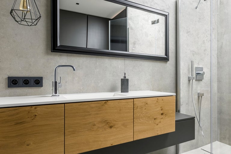 Modernes Badezimmer mit Waschtisch in Holzoptik, integriertem Waschbecken, Spiegel mit schwarzem Rahmen und angrenzender ebenerdiger Dusche.