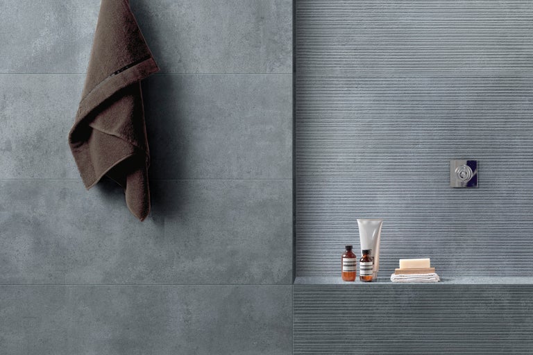 Modernes Badezimmer mit grauen Fliesen, Handtuch, Seife und Hautpflegeprodukten auf einem Regal