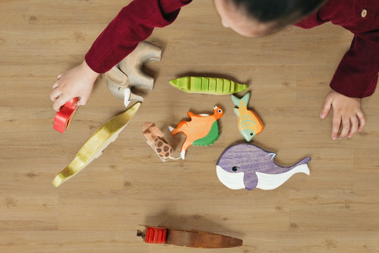 Draufsicht eines Kindes das mit hölzernen Spielzeugtieren und Fischen auf einem Holzboden spielt