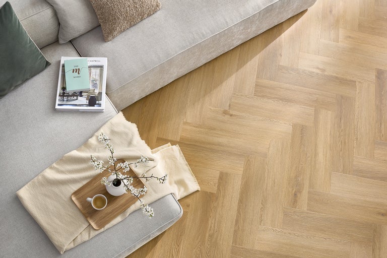 Ansicht eines Wohnzimmers mit Fischgrätenparkett, Sofa und Dekoration